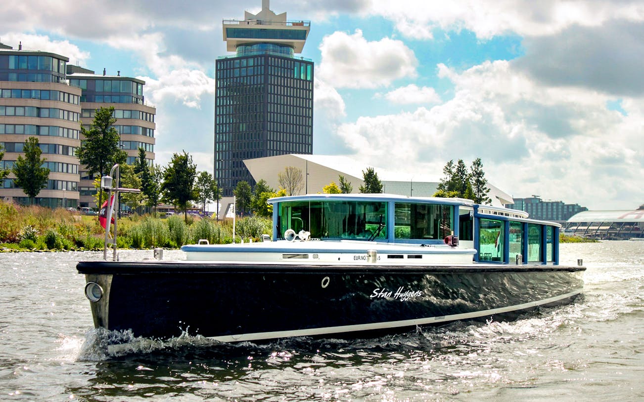 VIP Canal Cruise on Stan Huygens boat in Amsterdam with modern buildings in background.