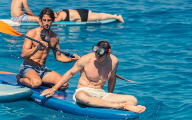 Tourists paddleboarding in Cala Bassa beach, Ibiza, Spain.