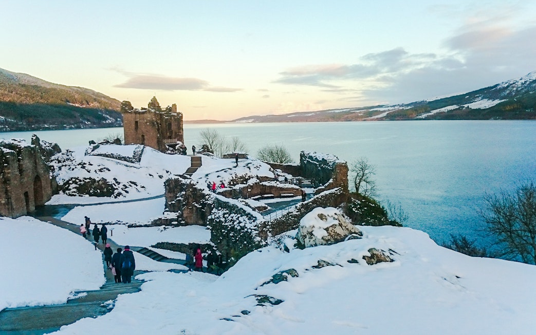 Urquhart Castle ruins overlooking snow-covered Loch Ness in winter.