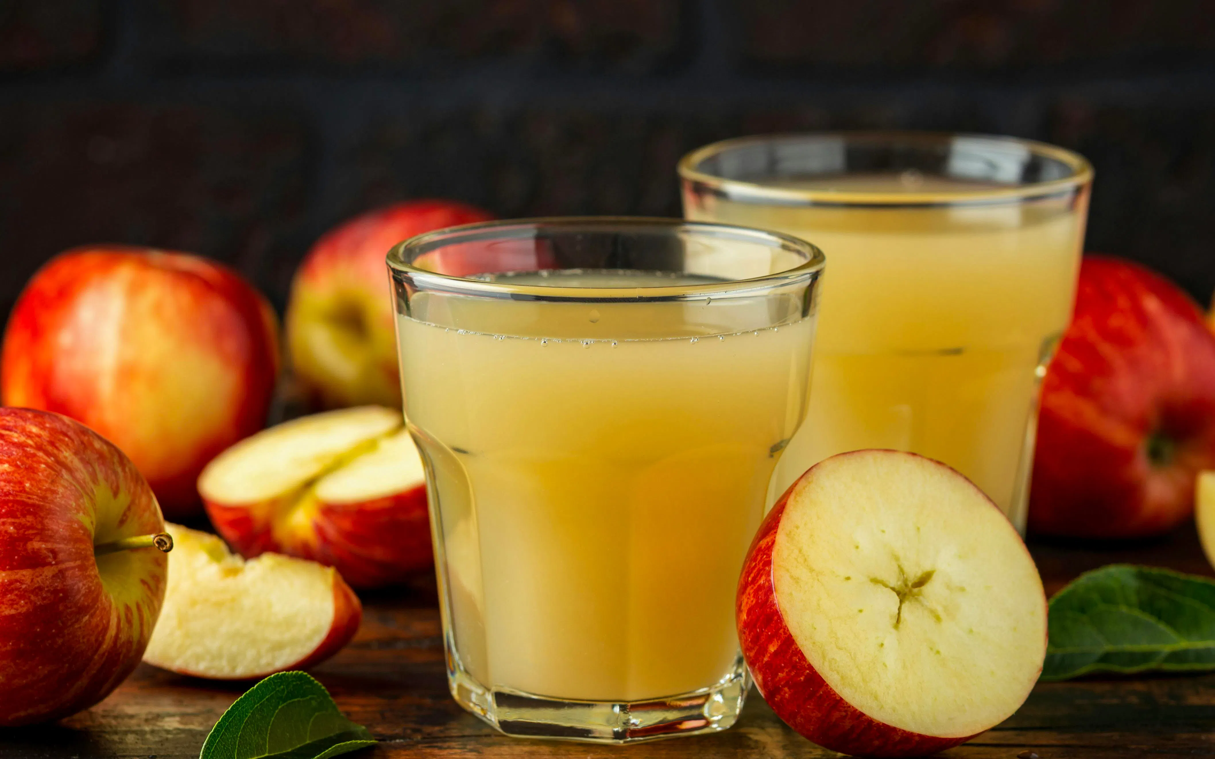 Apple juice in glass with fresh apples on rustic wooden table.