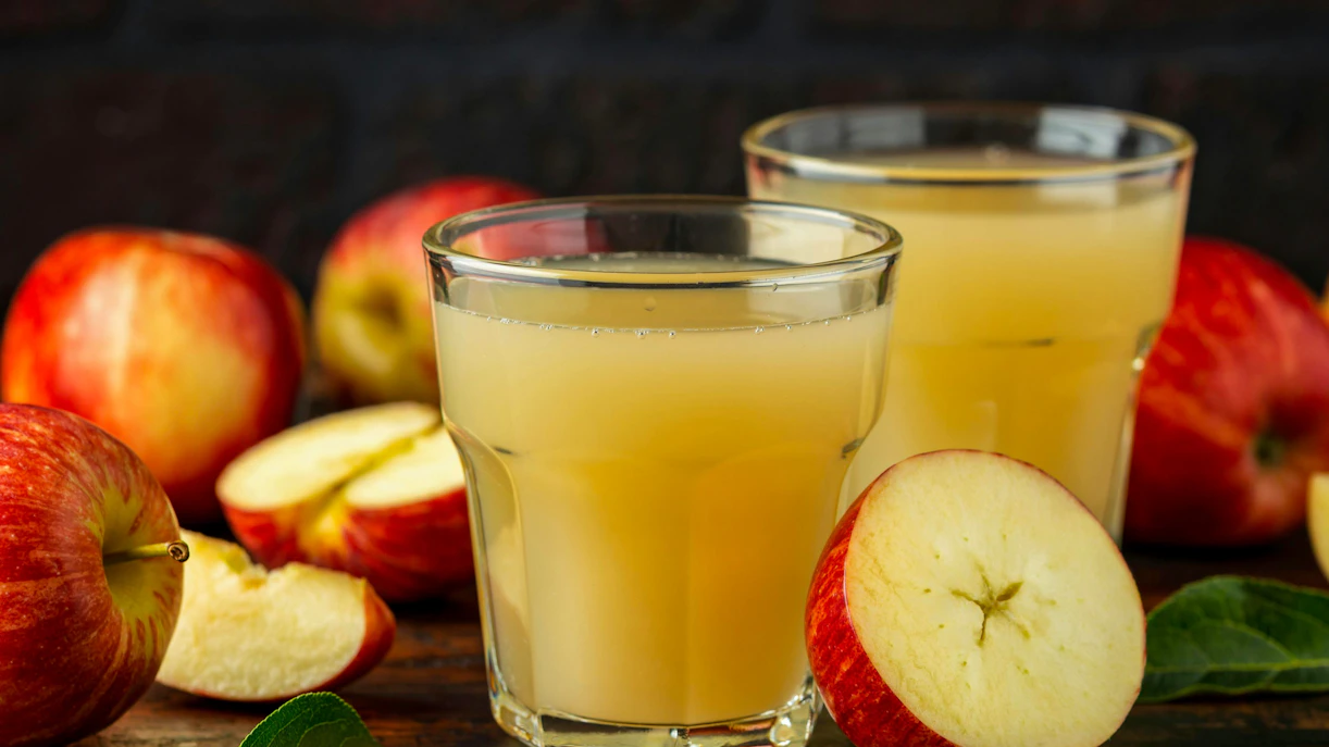 Apple juice in glass with fresh apples on rustic wooden table.