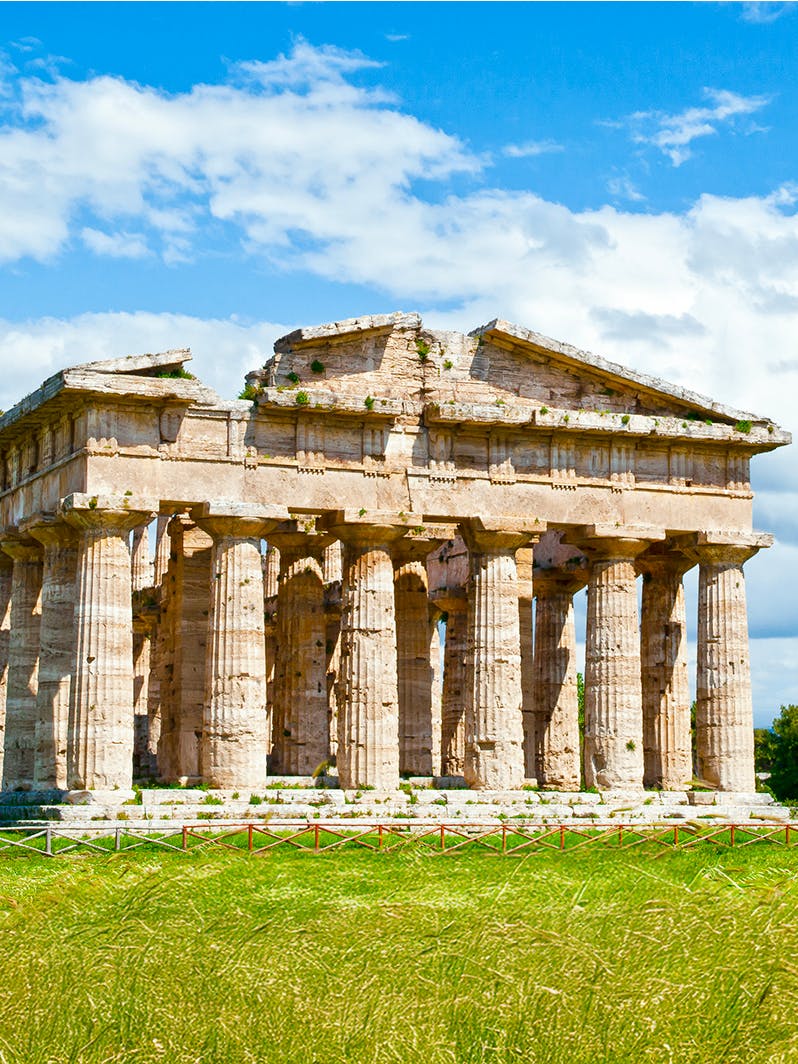 Temple of Poseidon ruins in Paestum, Italy, with ancient columns under a blue sky.