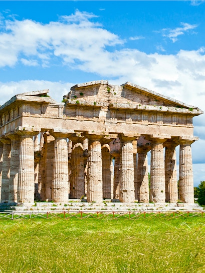 Temple of Poseidon ruins in Paestum, Italy, with ancient columns under a blue sky.