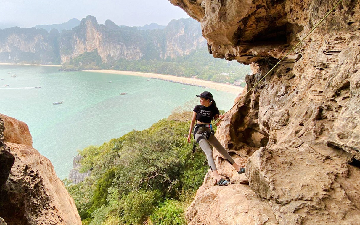 Tourist rock climbing at Railay Beach, Krabi with Real Rocks Climbing, overlooking the sea.