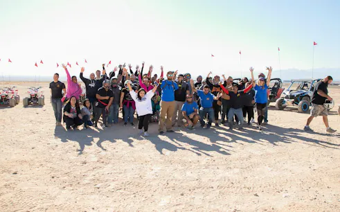 Group enjoying Las Vegas ATV tour on sand dunes with off-road vehicles in the background.