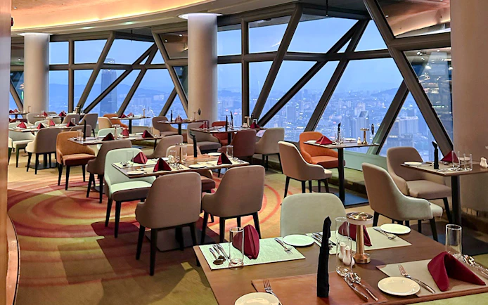 Dining tables set for lunch at ORBIT Revolving Dining, KL Tower, with city views.
