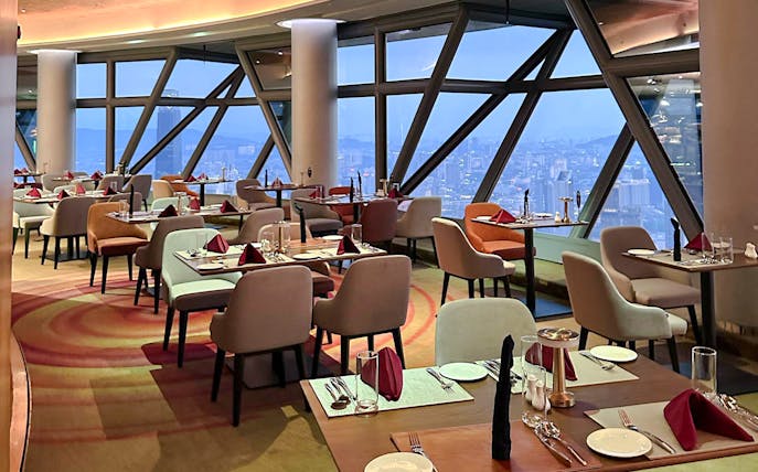 Dining tables set for lunch at ORBIT Revolving Dining, KL Tower, with city views.