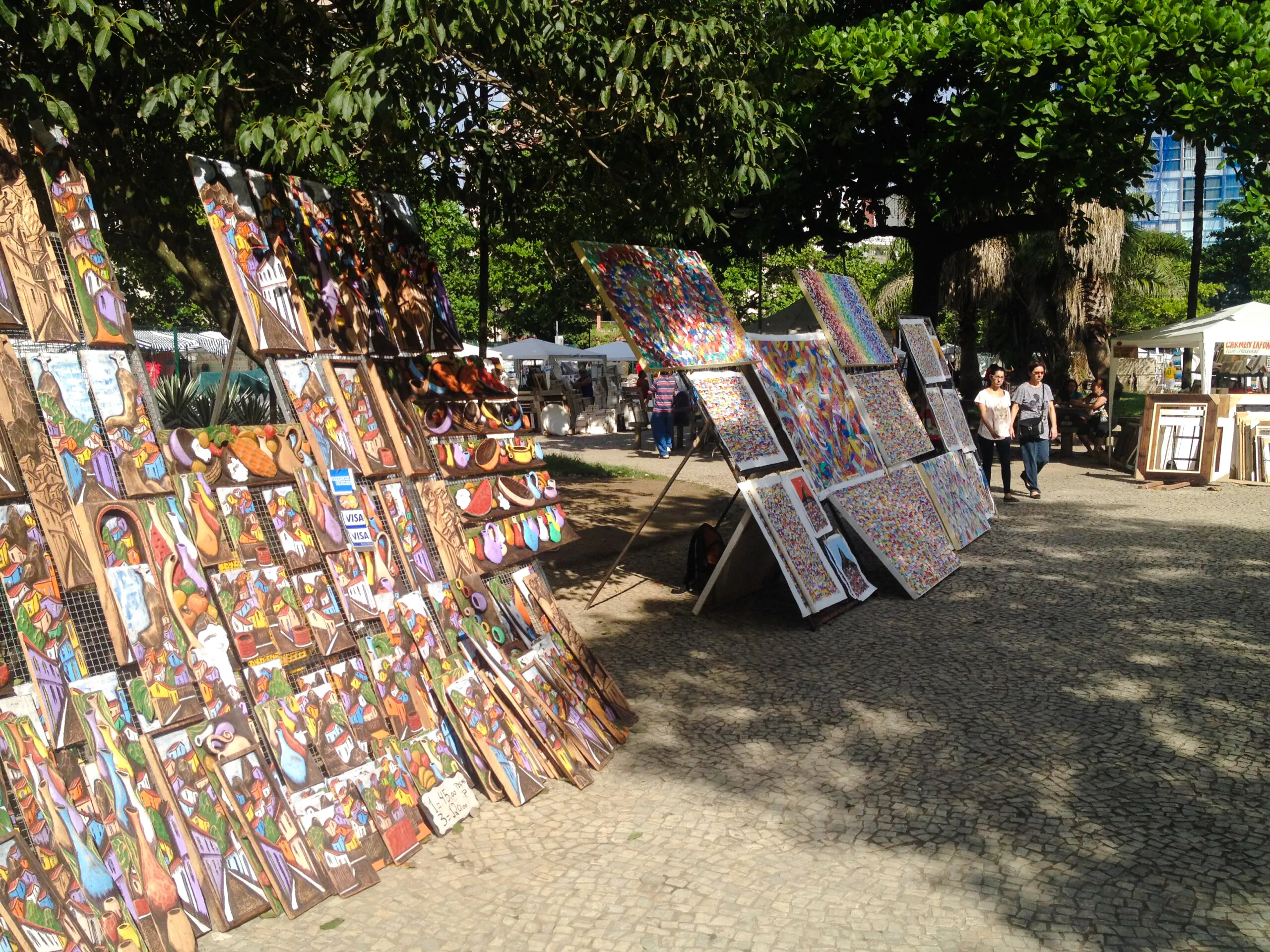 Art displays at Ipanema Street Market, Rio de Janeiro, with colorful paintings and local visitors.
