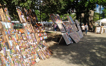 Art displays at Ipanema Street Market, Rio de Janeiro, with colorful paintings and local visitors.
