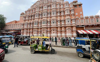 Hawa Mahal facade with rickshaws and visitors in Jaipur.