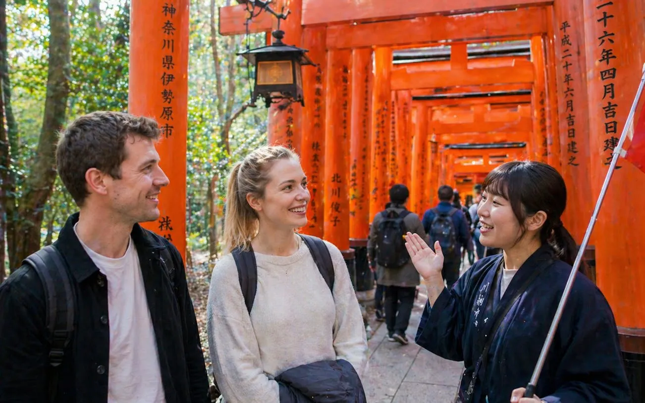 Tour guide leading visitors through Fushimi Inari Shrine's red torii gates in Kyoto.
