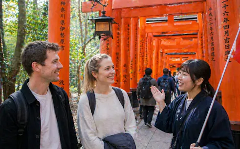 Tour guide leading visitors through Fushimi Inari Shrine's red torii gates in Kyoto.