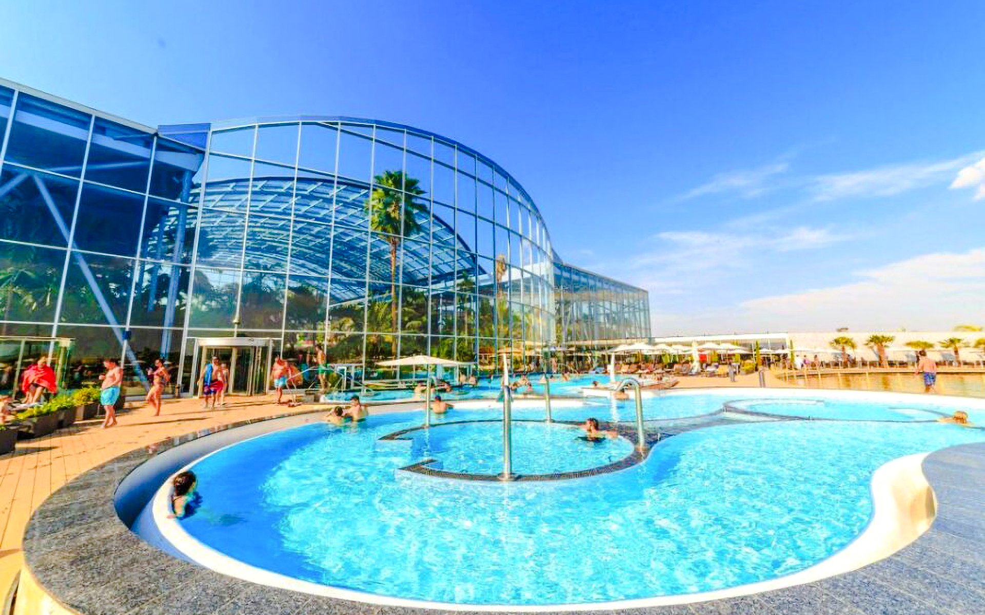 Therme Bucharest Spa pool with people swimming and lounging under a clear sky.