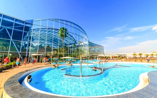 Therme Bucharest Spa pool with people swimming and lounging under a clear sky.