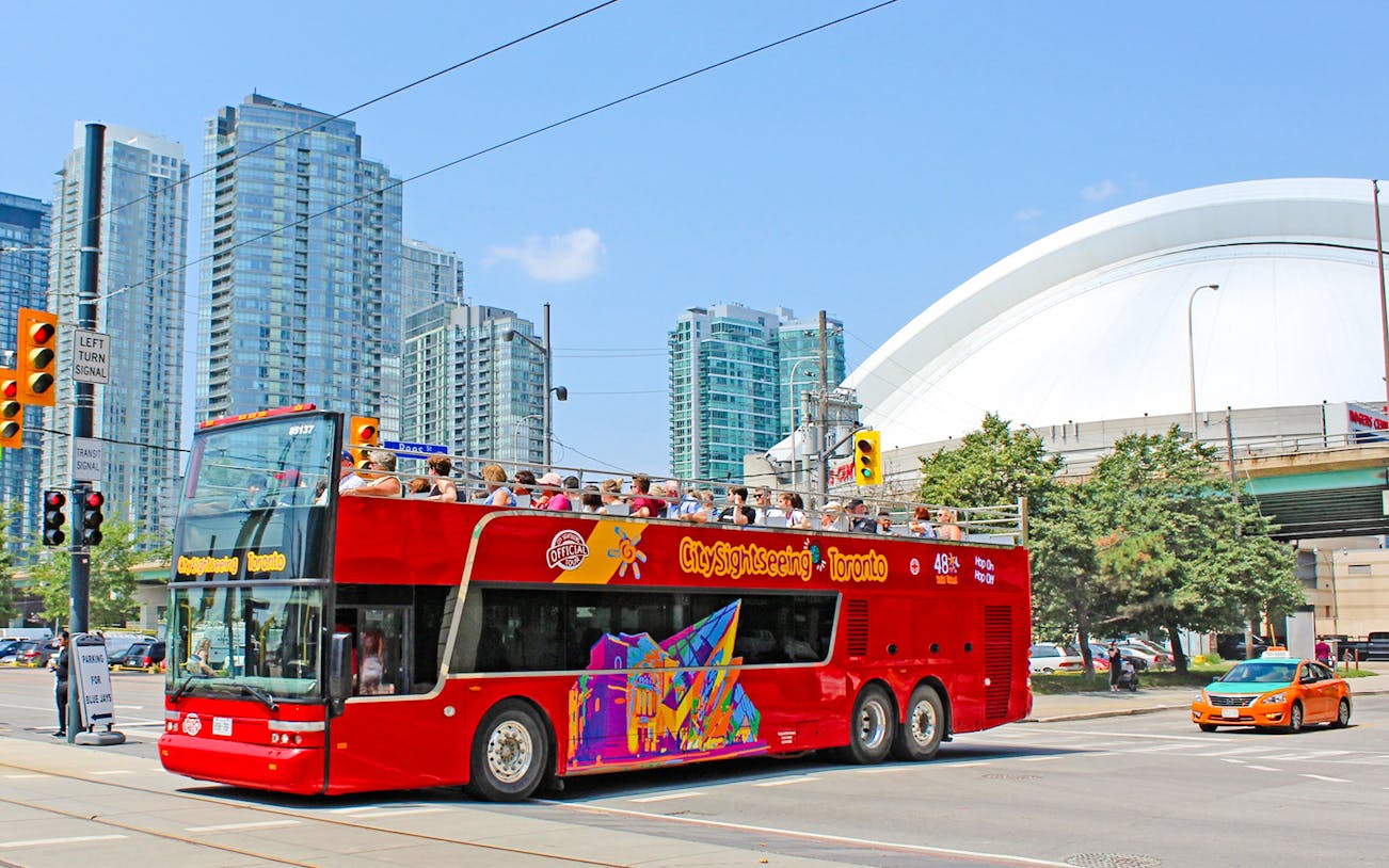 Open-top tour bus in Toronto with CN Tower and city skyline in the background.