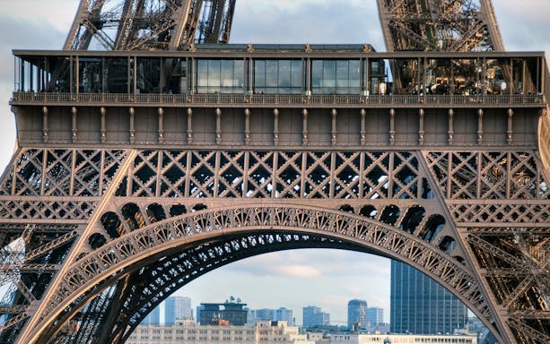 Eiffel Tower's iron lattice structure with Paris skyline in the background.