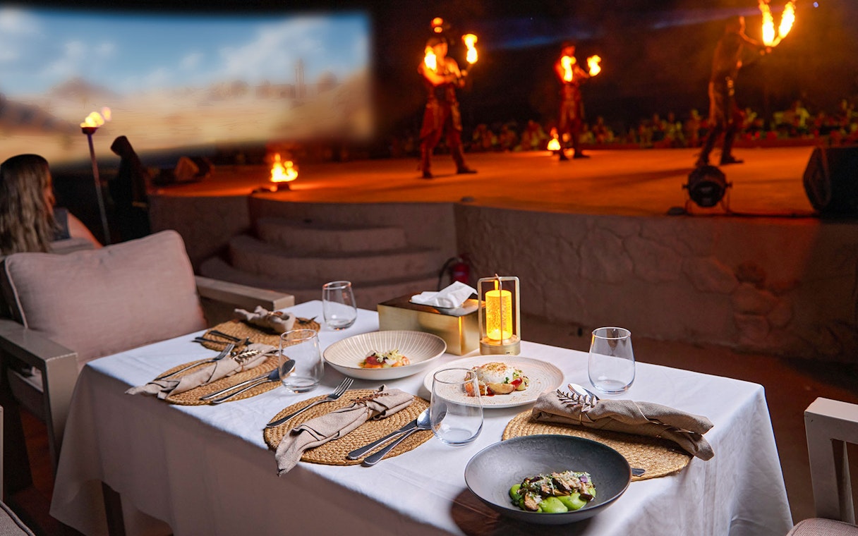 Dining setup with gourmet dishes at Noble Camp Desert Safari, fire performers in the background.