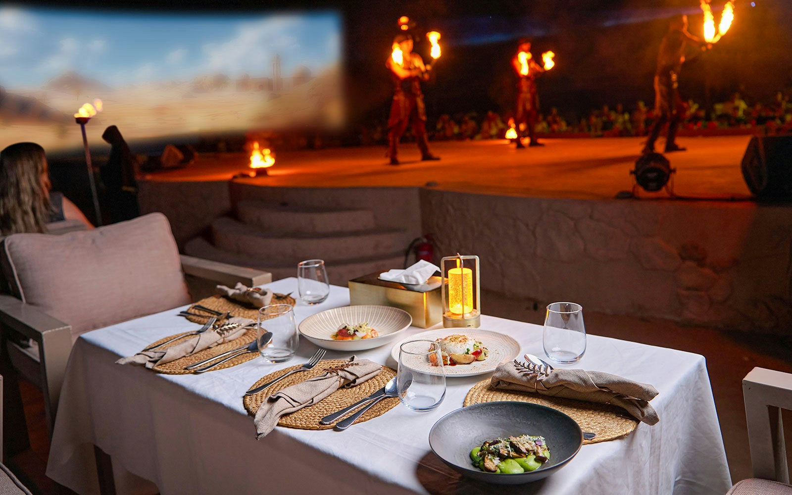 Dining setup with gourmet dishes at Noble Camp Desert Safari, fire performers in the background.