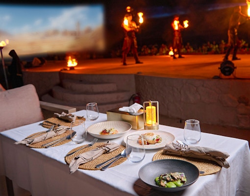 Dining setup with gourmet dishes at Noble Camp Desert Safari, fire performers in the background.