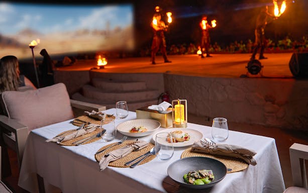 Dining setup with gourmet dishes at Noble Camp Desert Safari, fire performers in the background.
