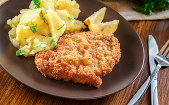 Viennese schnitzel with potato salad and lemon slices on a plate.