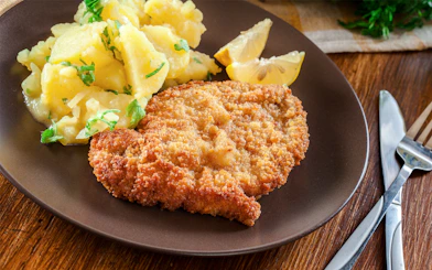 Viennese schnitzel with potato salad and lemon slices on a plate.