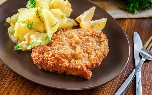 Viennese schnitzel with potato salad and lemon slices on a plate.