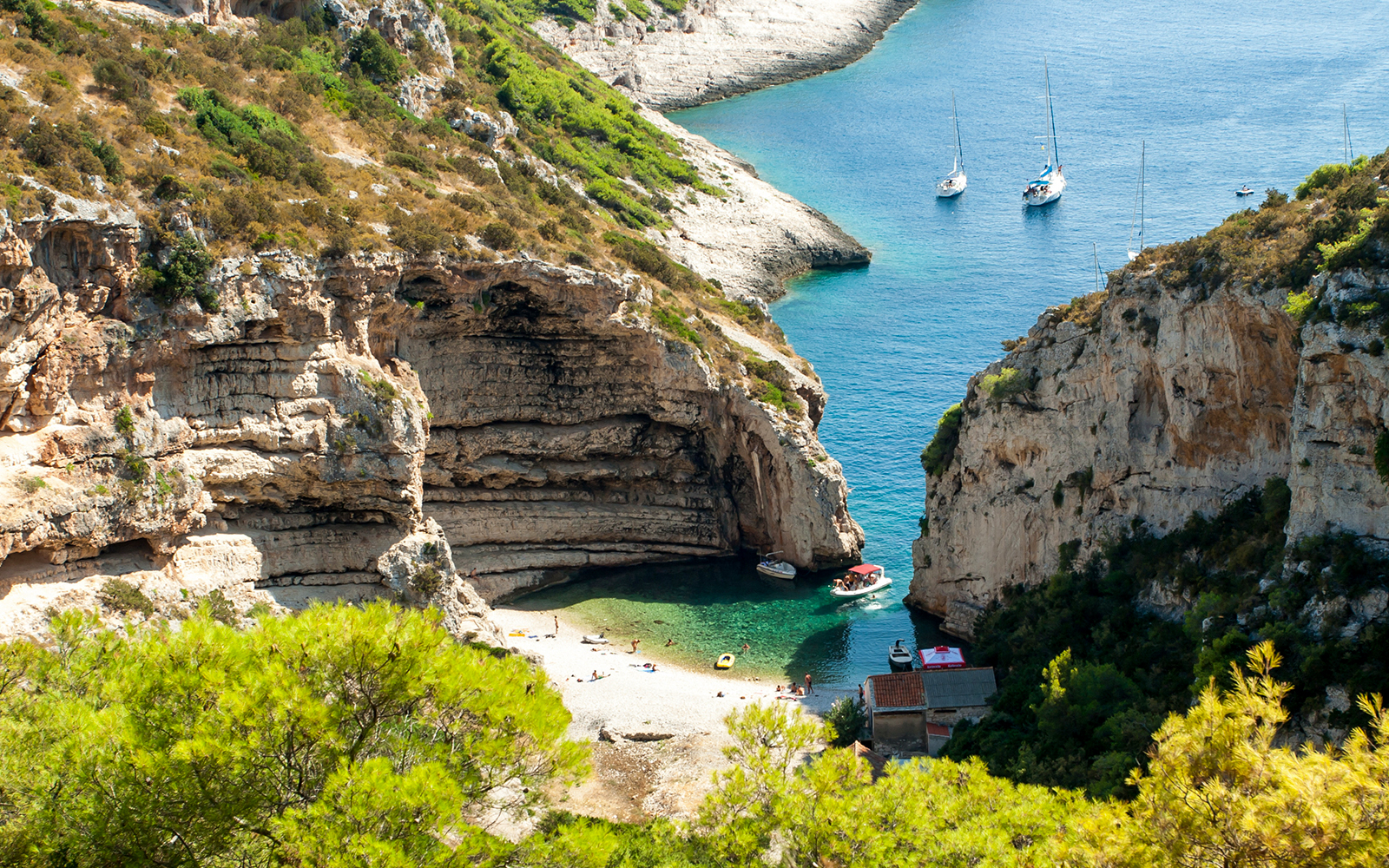 Stiniva Bay on Vis Island with boats and beachgoers surrounded by cliffs.