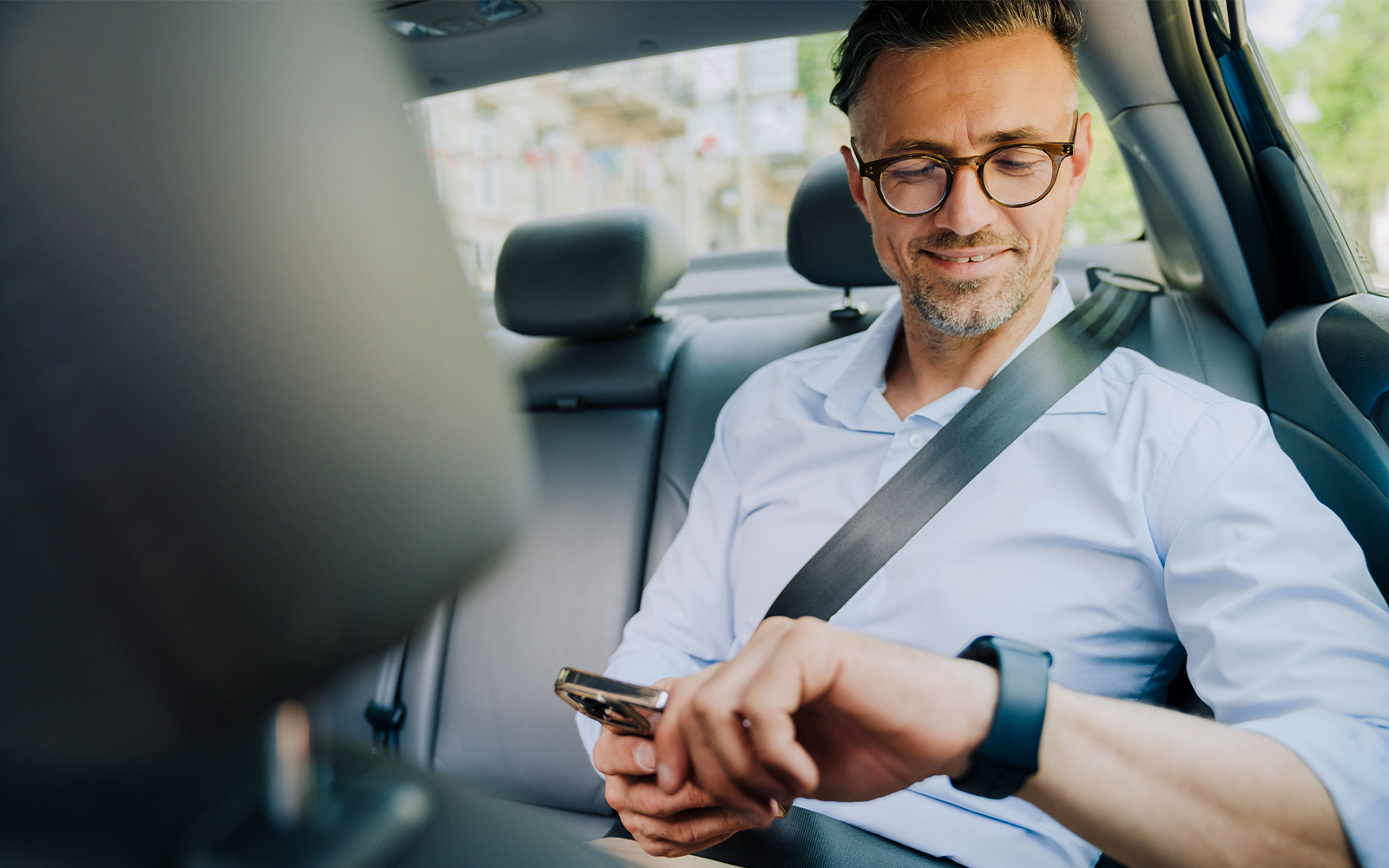 Man in car backseat checking phone and smartwatch.