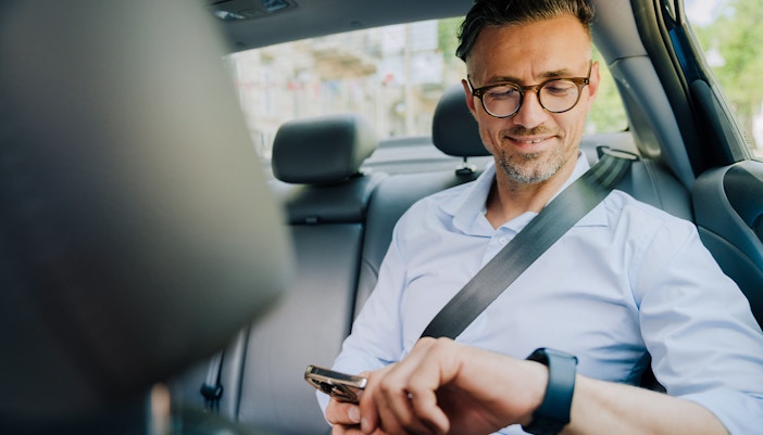 Man in car backseat checking phone and smartwatch.