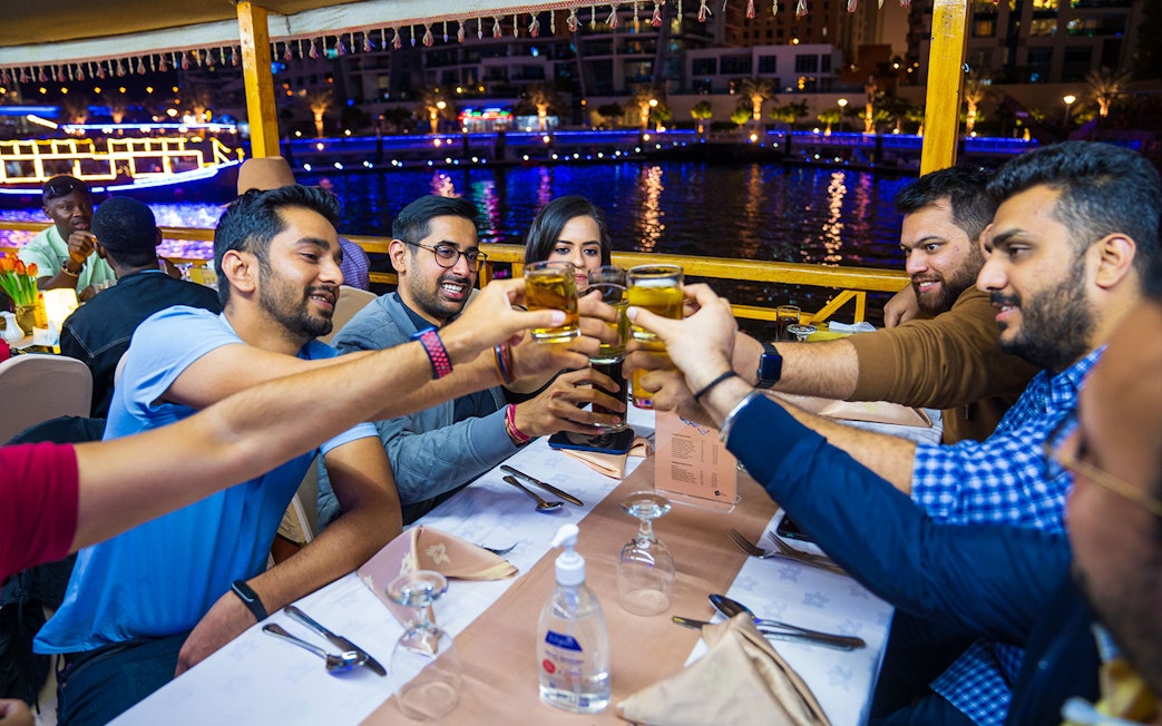 Guests toasting drinks on a Dhow Dinner Cruise in Dubai Creek at night.
