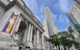 New York Public Library entrance with rainbow banner, skyscraper in background.