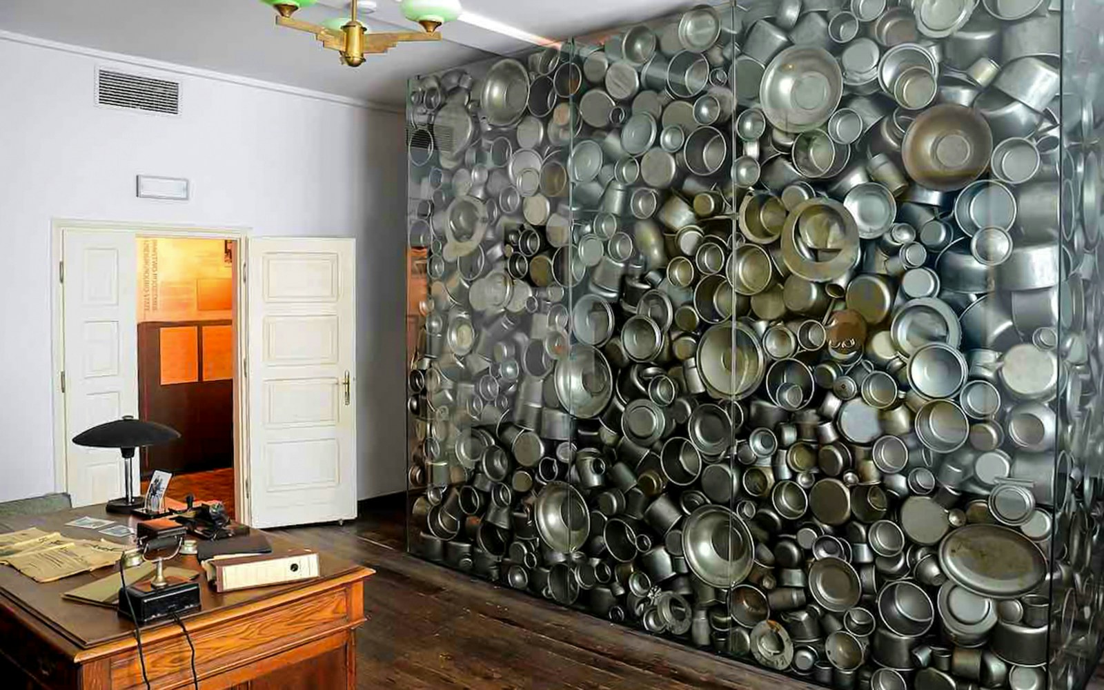 Oskar Schindler’s Factory interior with a wall of metal pots and a wooden desk.