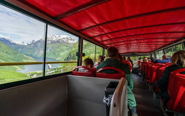 Passengers on Geiranger hop-on hop-off bus with fjord view through windows.