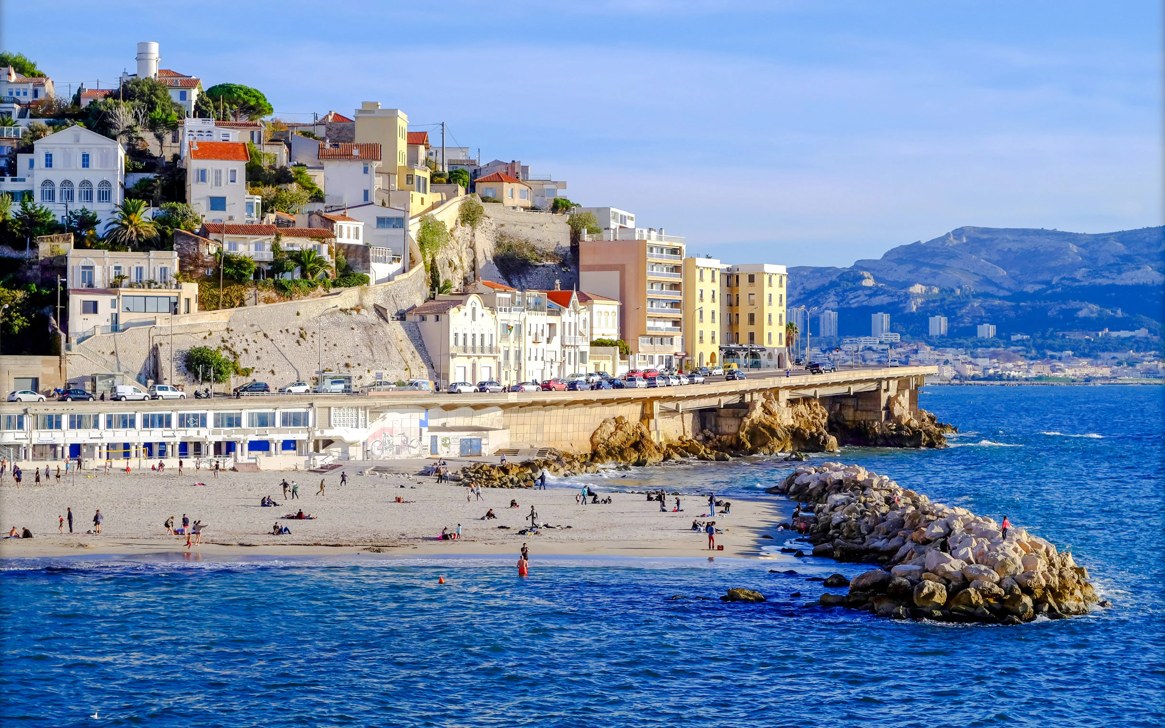 Plage du Prophète beach with people relaxing, Marseille coastline and buildings in the background.