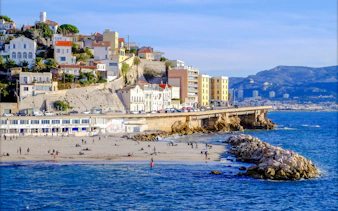 Plage du Prophète beach with people relaxing, Marseille coastline and buildings in the background.