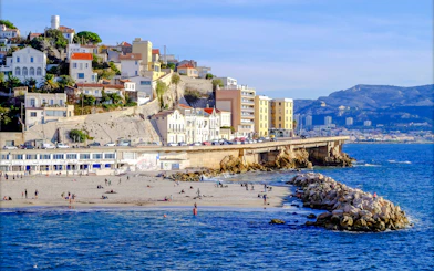 Plage du Prophète beach with people relaxing, Marseille coastline and buildings in the background.