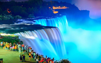 Crowd viewing illuminated Niagara Falls at night.