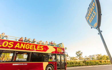 Open-top tour bus in Los Angeles near Beverly Hills sign.