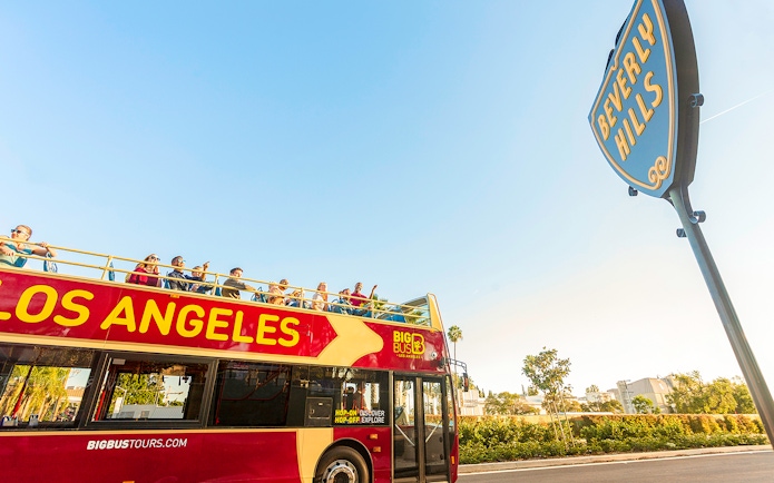 Open-top tour bus in Los Angeles near Beverly Hills sign.