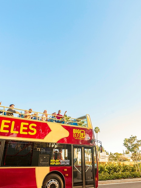 Open-top tour bus in Los Angeles near Beverly Hills sign.
