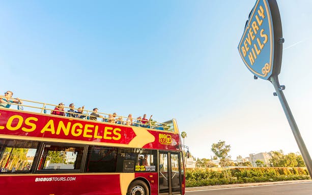 Open-top tour bus in Los Angeles near Beverly Hills sign.