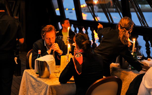Dinner guests on a Galleon Cruise in Venice with candlelit tables and water views.