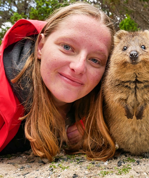 Person smiling with a quokka on Rottnest Island during a ferry and adventure boat tour.