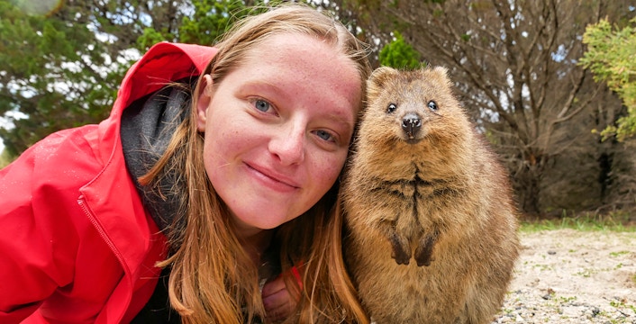 Person smiling with a quokka on Rottnest Island during a ferry and adventure boat tour.