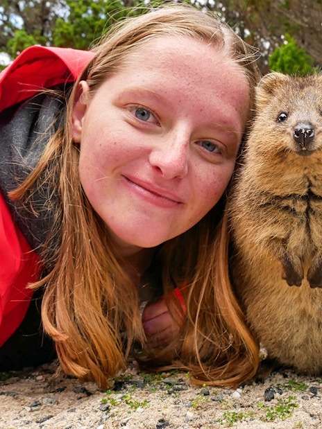 Person smiling with a quokka on Rottnest Island during a ferry and adventure boat tour.
