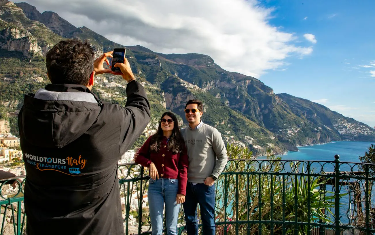 Tourists posing for a photo with scenic view of Amalfi Coast cliffs and sea in the background.