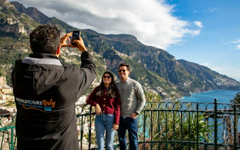 Tourists posing for a photo with scenic view of Amalfi Coast cliffs and sea in the background.