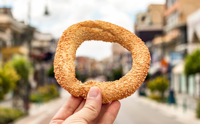 Sesame-covered bread ring held in hand on an Athens street during vegan tour.