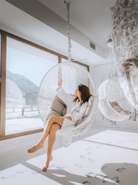 Person relaxing in a hanging chair at QC Terme Chamonix spa with snowy mountain view.